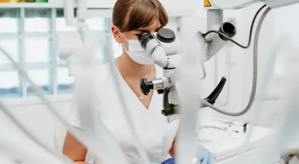 Dentystka pod mikroskopem bada, czy plomba światłoutwardzalna może wypaść. Precyzyjna praca w gabinecie.