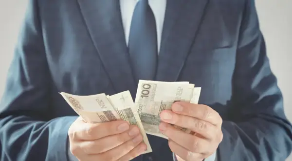 Mężczyzna w garniturze liczy polskie banknoty 100 zł. To zabezpieczenie należytego wykonania umowy.