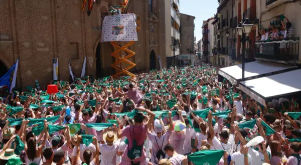 Multitud celebra el programa fiestas Huesca, agitando pañuelos verdes. Un cartel anuncia "25".