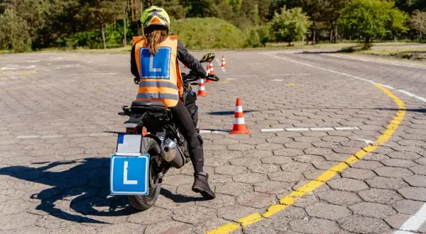 Osoba na motocyklu z tablicą "L" i kamizelką odblaskową na placu manewrowym.