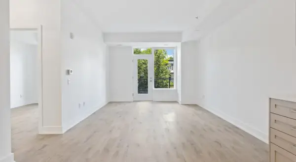 Amplio salón diáfano con suelo de madera clara y puerta acristalada que da a un balcón con vistas a árboles. Ideal para vender piso heredado antes de 5 años.