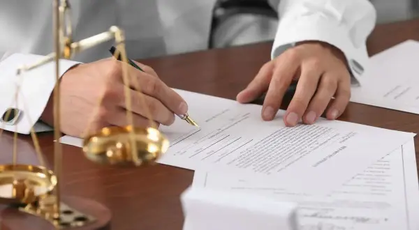 Prawnik podpisuje dokumenty, gdzie rozstrzygane jest prawo do zachowku a testament. Waga sprawiedliwości symbolizuje równowagę.