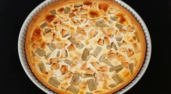 Tarte rhubarbe pomme dorée, garnie de morceaux de fruits et d'une crème onctueuse, prête à être dégustée.