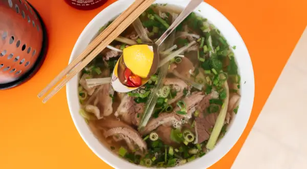 Aromatyczne wietnamskie jedzenie: miska pho z wołowiną, makaronem ryżowym, ziołami i plasterkami chili na łyżce.