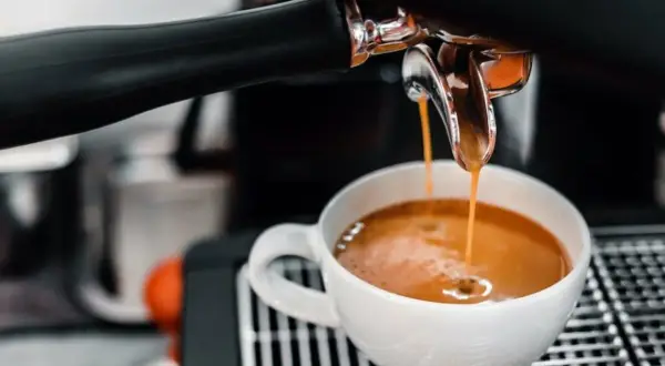 En espressomaskin hjälper till att brygga espresso. Varm, gyllene kaffe rinner ner i en vit kopp.