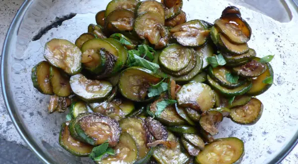 Zucchine alla scapece, fritte e condite con aceto e menta, in una ciotola di vetro.