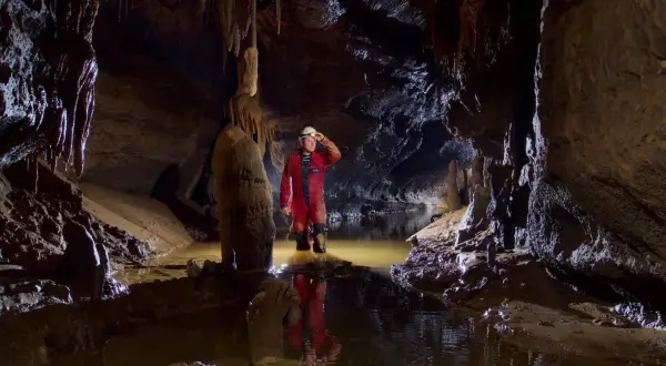 Eksplorator w czerwonym kombinezonie w jaskini z wodą. To jest właśnie speleologia co to – badanie podziemnych światów.