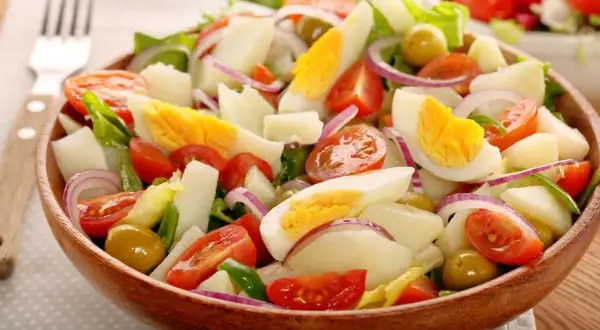 Ensalada de patatas de verano con huevo duro, tomates, aceitunas y cebolla morada en un cuenco de madera.