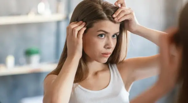Junge Frau prüft im Spiegel ihre Haare und fragt sich, wie viel wachsen Haare im Monat.