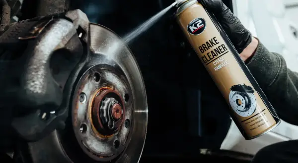 Czyszczenie zużytych tarcz hamulcowych preparatem K2 Brake Cleaner. Widoczny rozpylacz i brudny element układu hamulcowego.
