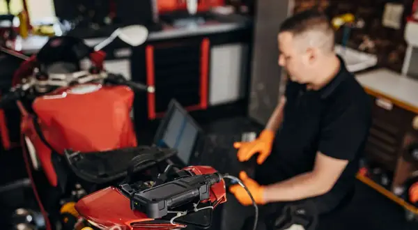 Mecánico con guantes naranjas usa un portátil para ver cómo se puede reprogramar una moto roja.