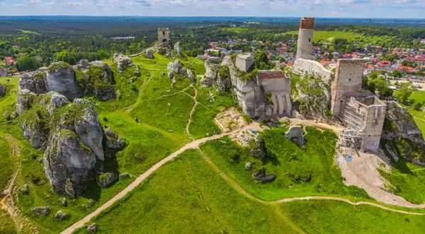 Ruiny zamków na wapiennych skałach w parku krajobrazowym Orlich Gniazd, otoczone zielonymi wzgórzami i lasami.