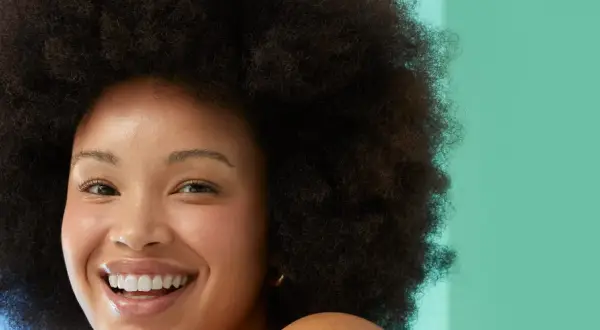 Rostro sonriente de mujer con afro, piel radiante. Evita la glicerina, es mala para la piel.