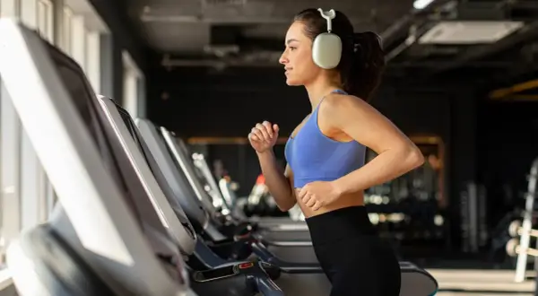 Junge Frau läuft auf Laufband im Fitnessstudio, motiviert für Fitness und Abnehmen.