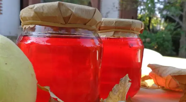 Due barattoli di gelatina di mele cotogne, con mele e foglie autunnali.