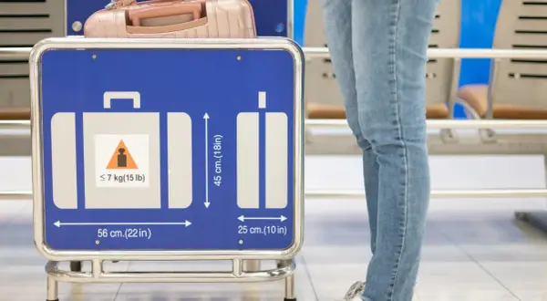 Person mit Handgepäck vor einem Schild mit Gepäckmaßen und Gewichtsbeschränkung.