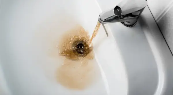 Acqua gialla dalla caldaia che scorre nel lavandino, creando un alone marrone.