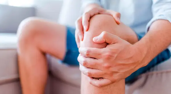 Mann hält sein Knie, das einen stechenden Schmerz im Knie anzeigt.