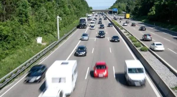 Autobahn mit vielen Autos und einem Wohnwagen. Ein Schild am Horizont deutet das ende autobahn schild an.