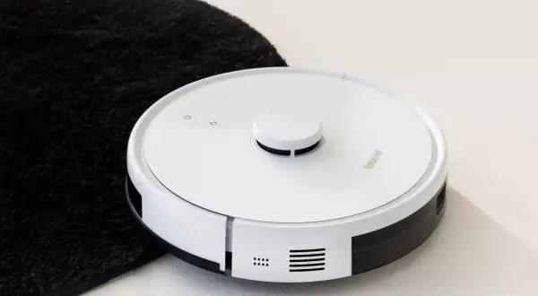 Biały robot sprzątający obok czarnego dywanika. Jego moc ssania odkurzacza poradzi sobie z każdym brudem.