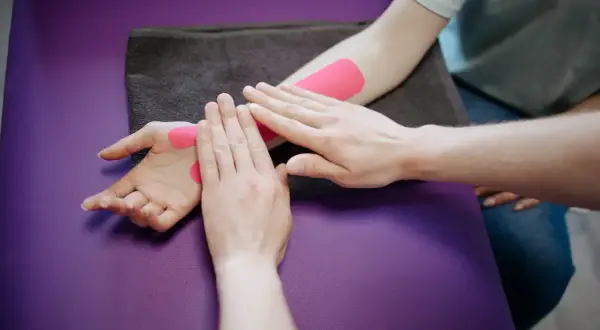 Fizjoterapeuta aplikuje taśmy kinezjotaping na nadgarstek pacjenta. Długość rehabilitacji po złamaniu nadgarstka zależy od wielu czynników.