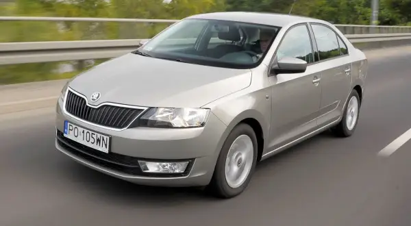 Srebrna Skoda Rapid jedzie po drodze. Kierowca jest widoczny za kierownicą. Wiele osób szuka skoda rapid opinie przed zakupem.