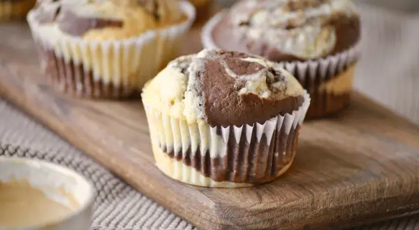 Zwei leckere Marmor Muffins auf einem Holzbrett, daneben eine Tasse Kaffee.