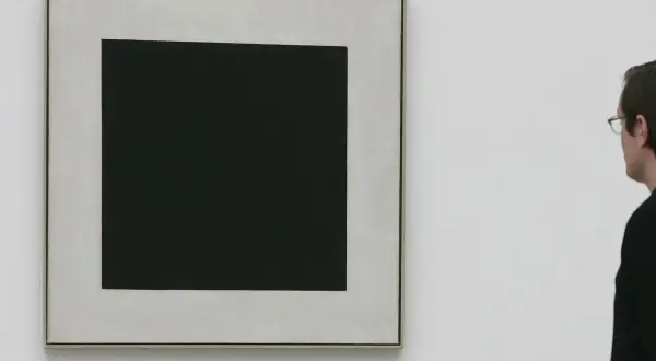 Ein Mann betrachtet ein schwarzes Quadrat auf hellem Grund. Die schlichte Komposition lässt Raum für Interpretationen, die schwarzes Quadrat Bedeutung.