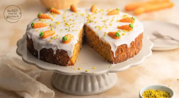 Ein saftiger karottenkuchen mit cremigem frosting, dekoriert mit kleinen Marzipan-Karotten und gehackten Pistazien.