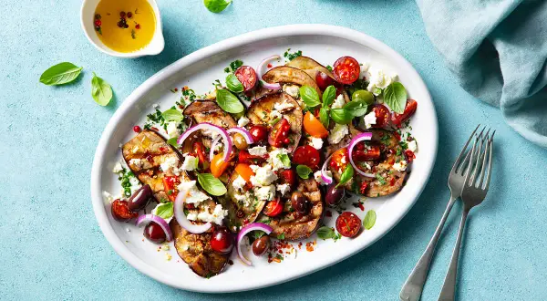 Gegrillte Auberginenscheiben mit Tomaten, Oliven, Feta und Basilikum – ein köstliches Beispiel für mediterrane Rezepte.