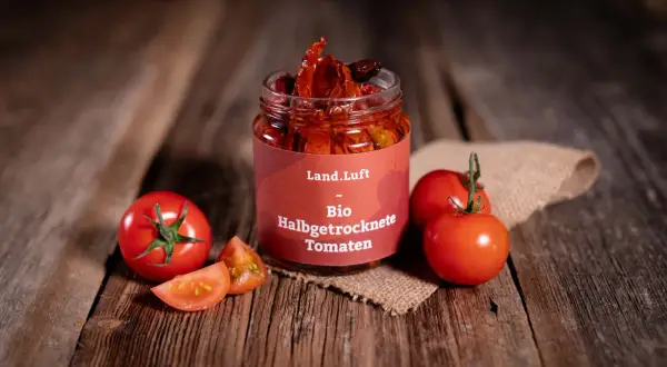 Glas mit halbgetrockneten Tomaten, frische Tomaten und Scheiben auf Holzhintergrund.