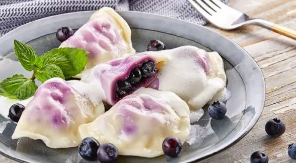 Pyszne pierogi z jagodami, polane śmietaną, ozdobione miętą i świeżymi owocami. Idealne na deser!