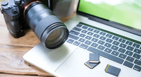 Aparat fotograficzny i karty pamięci leżą obok laptopa, gotowe do akcji. Dowiedz się, jak zgrać zdjęcia z aparatu na laptop.