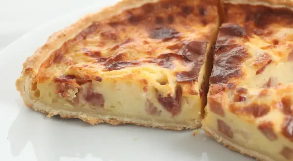 Un trozo de quiche de verduras con trocitos de bacon, horneado hasta dorarse.