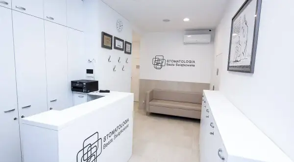 Nowoczesne wnętrze recepcji stomatologicznej z białym lady, kanapą i logo kliniki.