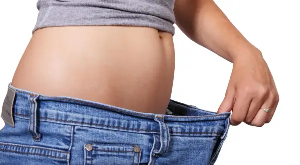 En kvinna håller upp sina jeans som är för stora, ett tecken på att hon lyckats gå ner i vikt efter graviditet.