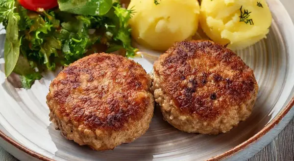 Dwa apetyczne kotlety mielone z airfryer, podane z ziemniakami i świeżą sałatką.