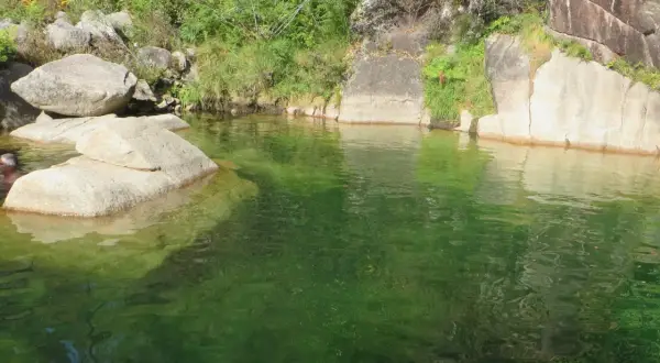 Un hombre se baña en la poza de agua verde de la corga da fecha, rodeada de rocas y vegetación.