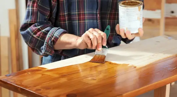 Mano che applica mordente su legno con pennello. Il mordente significato è dare colore e profondità al legno.