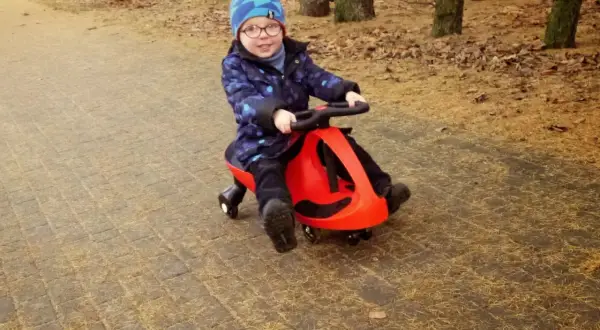 Uśmiechnięty chłopiec w czapce jedzie na czerwonym twistcarze. Od jakiego wieku można zacząć zabawę? Odpowiedź znajdziesz na blogu!