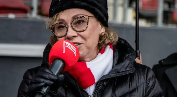 Prezes Cracovii w czapce i szaliku klubu, z mikrofonem w ręku, przemawia do zgromadzonych.
