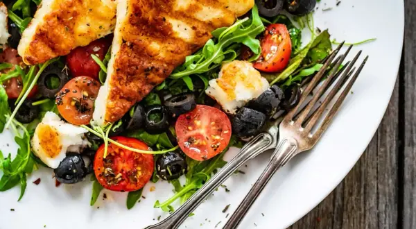 Pyszna sałatka z grillowanym halloumi, pomidorkami koktajlowymi i czarnymi oliwkami na rukoli. Idealna na lekki posiłek.