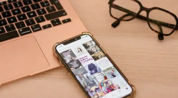 Telefon z uszkodzonym ekranem obok laptopa i okularów. Szukasz sposobu, jak wyświetlić uszkodzony ekran telefonu na komputerze?