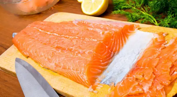 Un beau filet de truite saumonée prêt à être transformé en gravlax, avec du citron, de l'aneth et de l'ail en arrière-plan.