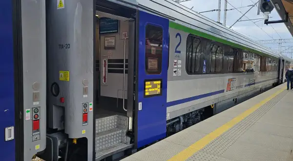 Eurocity train z otwartymi drzwiami na peronie. Widoczne schody, oznaczenia wagonu i fragmenty wnętrza.