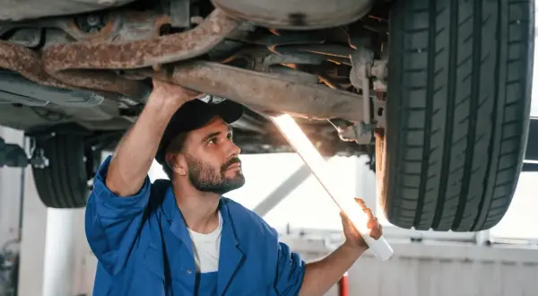 Mechanik z latarką bada podwozie auta. Upewnia się, że nie ma **braku przeglądu powyżej 30 dni**, by zapewnić bezpieczeństwo.