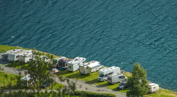 Un garaje al aire libre con varias caravanas y autocaravanas aparcadas junto a un lago azul.