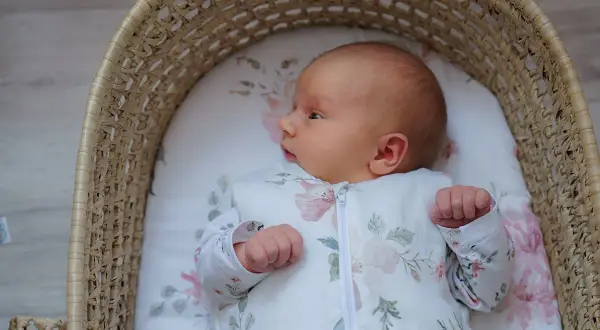 Malutkie dziecko w śpiworku z motywem kwiatowym leży w wiklinowym koszu. Czy to sids? Nie, to po prostu słodki bobas.