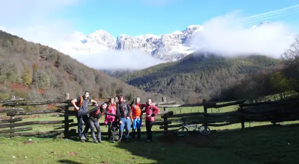 Grupo de senderistas posa junto a un cercado de madera en la ruta Soto de Sajambre-Vegabaño, con montañas nevadas al fondo.
