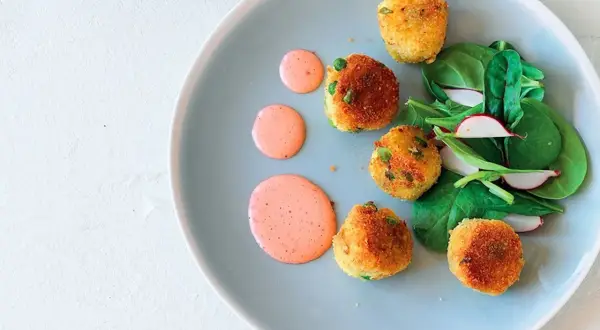 Deliziose polpette di verdure dorate, servite con insalata fresca e salsa rosa su un piatto azzurro.